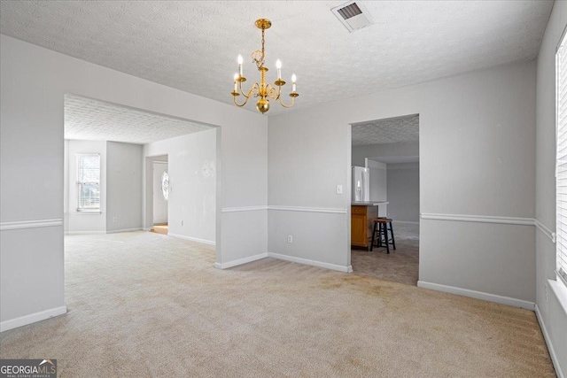 carpeted empty room featuring a textured ceiling and a notable chandelier