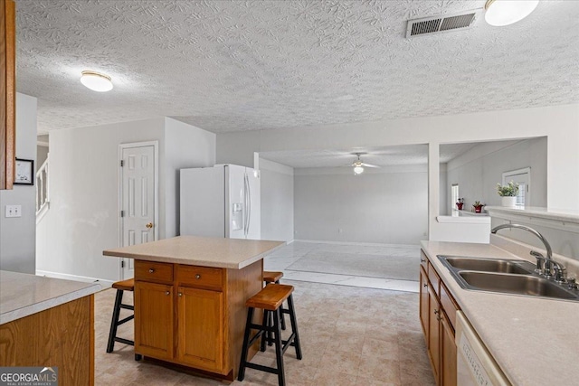 kitchen with a breakfast bar, sink, a kitchen island, ceiling fan, and white refrigerator with ice dispenser