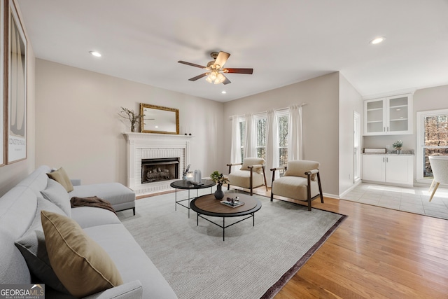 living room with a brick fireplace, light hardwood / wood-style floors, and ceiling fan