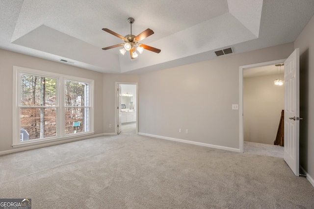 unfurnished bedroom with a tray ceiling, carpet floors, a textured ceiling, and ensuite bathroom