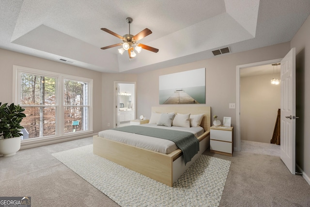 bedroom with connected bathroom, a tray ceiling, light colored carpet, and a textured ceiling