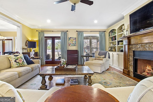 living room with crown molding, light hardwood / wood-style floors, built in features, a fireplace, and ceiling fan with notable chandelier