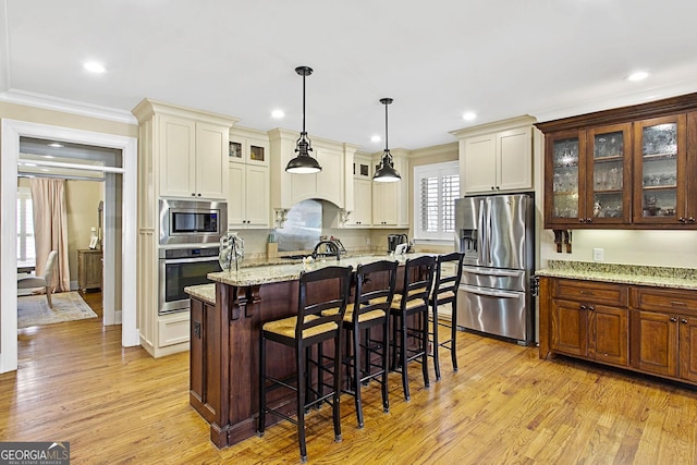 kitchen featuring light hardwood / wood-style flooring, appliances with stainless steel finishes, an island with sink, pendant lighting, and light stone countertops