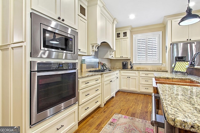 kitchen featuring premium range hood, stainless steel appliances, light stone countertops, decorative light fixtures, and light wood-type flooring