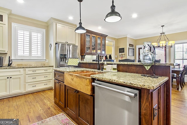 kitchen with pendant lighting, ornamental molding, appliances with stainless steel finishes, and an island with sink