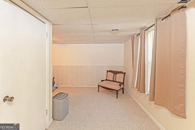 living area featuring carpet flooring, a paneled ceiling, and wooden walls