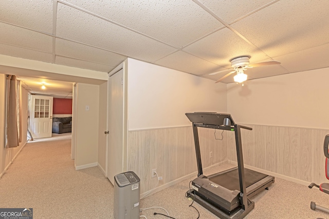 exercise room featuring light carpet, a paneled ceiling, ceiling fan, and wood walls