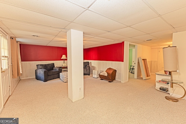 basement featuring carpet floors, a paneled ceiling, and wood walls