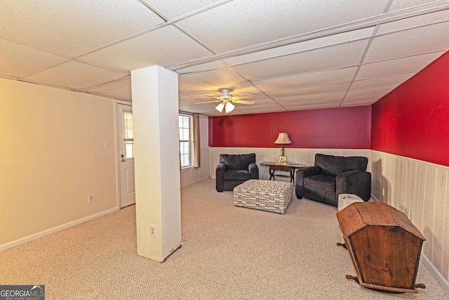 carpeted living room featuring ceiling fan, wood walls, and a drop ceiling