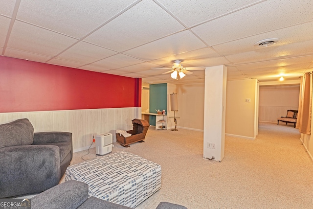 carpeted living room with a paneled ceiling, wooden walls, and ceiling fan