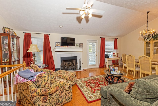 living room with lofted ceiling, a tiled fireplace, light hardwood / wood-style floors, and a textured ceiling