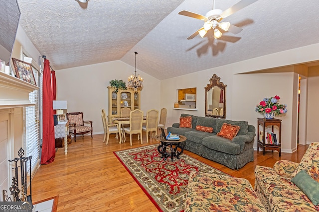 living room with hardwood / wood-style flooring, lofted ceiling, ceiling fan with notable chandelier, and a textured ceiling