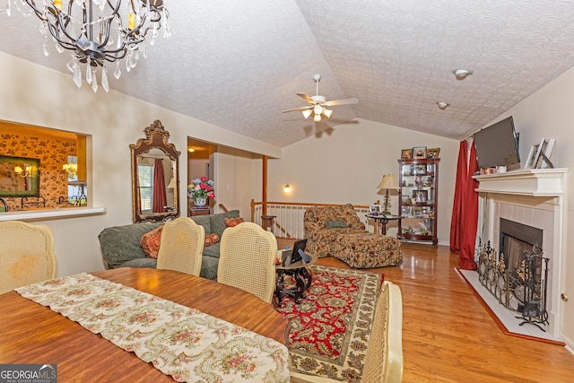 dining room featuring lofted ceiling, light hardwood / wood-style flooring, a textured ceiling, ceiling fan, and a tiled fireplace