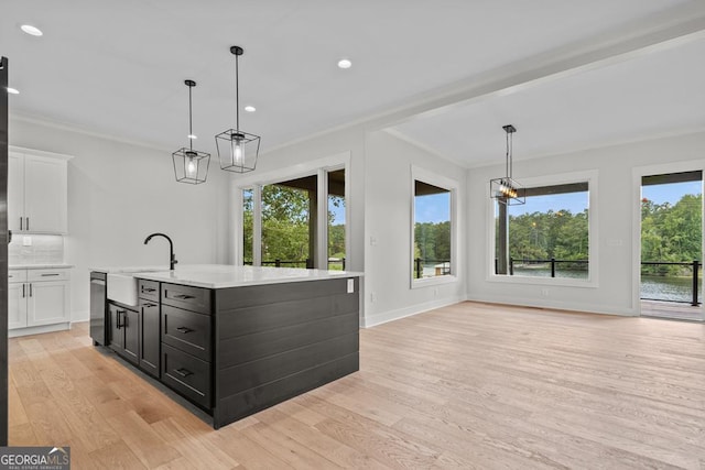 kitchen featuring pendant lighting, sink, light hardwood / wood-style floors, an island with sink, and white cabinets