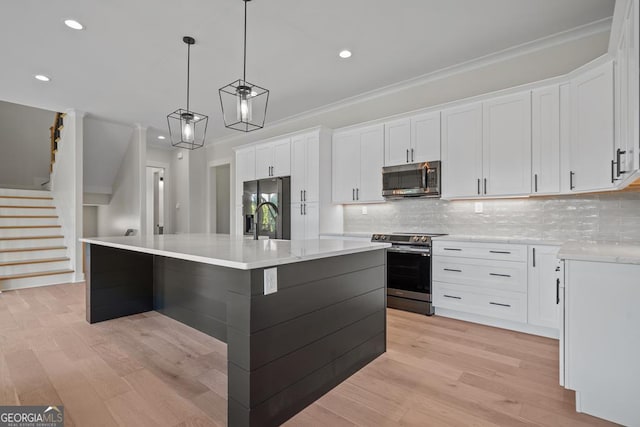 kitchen featuring light hardwood / wood-style flooring, white cabinetry, stainless steel appliances, an island with sink, and decorative light fixtures