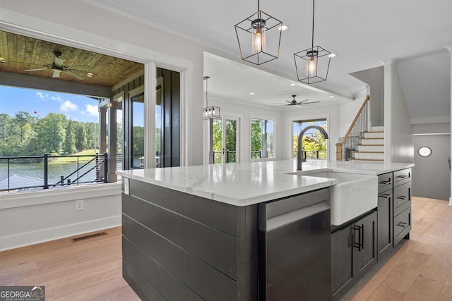 kitchen with hanging light fixtures, an island with sink, dishwasher, and light hardwood / wood-style flooring