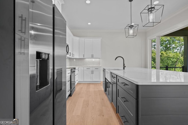 kitchen with ornamental molding, stainless steel appliances, a center island with sink, and white cabinets