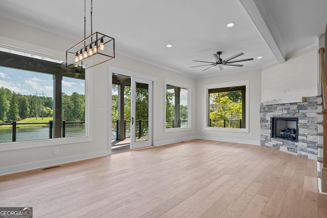 unfurnished living room featuring crown molding, ceiling fan, a water view, a stone fireplace, and light wood-type flooring