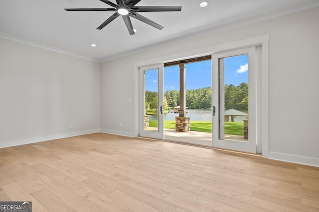 spare room with crown molding, light wood-type flooring, ceiling fan, and a water view