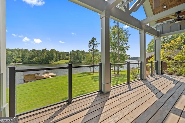 wooden terrace with a water view, ceiling fan, and a lawn