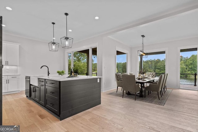 kitchen with a kitchen island with sink, hanging light fixtures, white cabinets, and light wood-type flooring