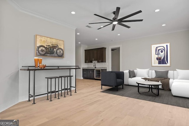 living room with indoor bar, beverage cooler, ceiling fan, light hardwood / wood-style floors, and crown molding