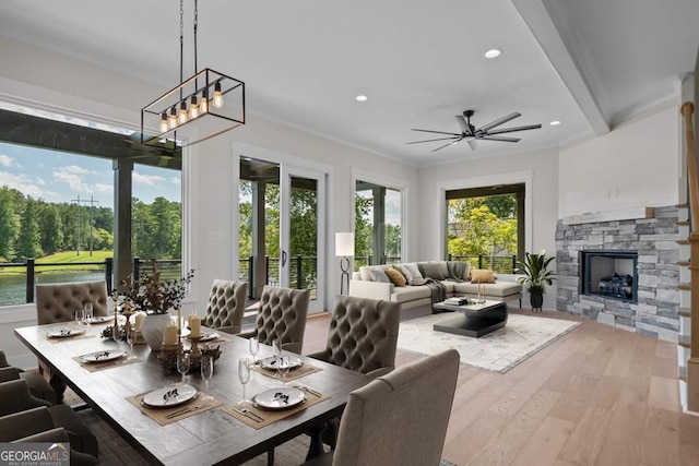 sunroom with a water view, ceiling fan, a stone fireplace, and beamed ceiling