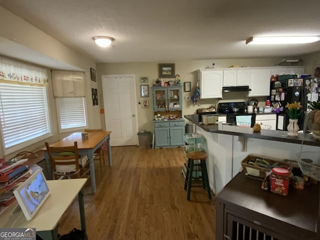 kitchen featuring a breakfast bar area, light hardwood / wood-style flooring, range, white cabinetry, and black refrigerator