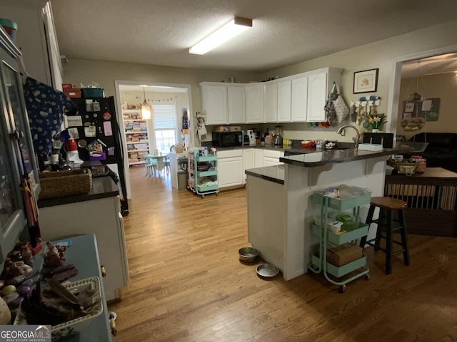 kitchen featuring light wood-type flooring, a breakfast bar area, white cabinets, kitchen peninsula, and a textured ceiling