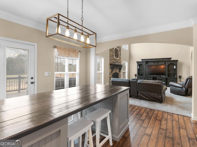 dining area featuring dark hardwood / wood-style flooring, crown molding, and a stone fireplace