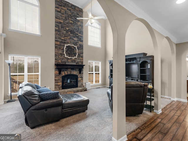 living room with a stone fireplace, ornamental molding, a towering ceiling, ceiling fan, and hardwood / wood-style floors