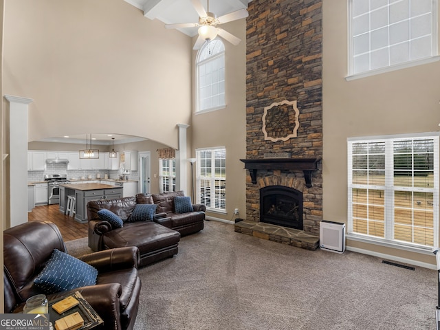 living room featuring ceiling fan, a stone fireplace, carpet, and a high ceiling