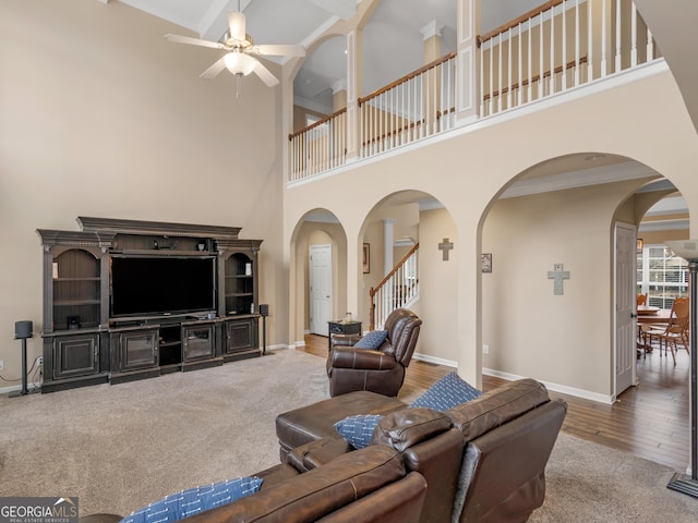 living room with crown molding, ceiling fan, wood-type flooring, and a high ceiling