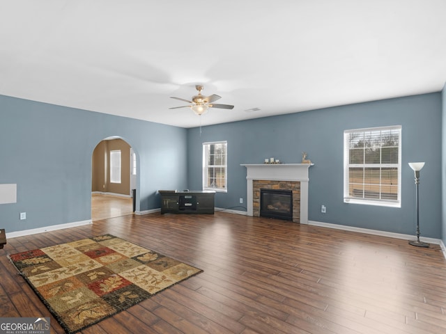 unfurnished living room featuring a stone fireplace, dark hardwood / wood-style floors, and ceiling fan