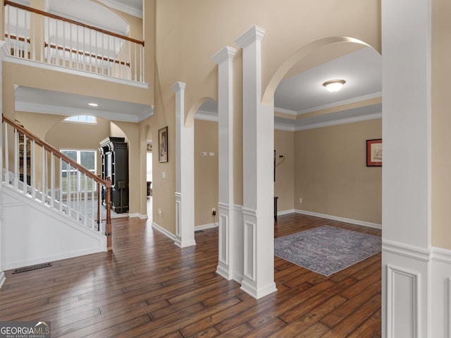 entrance foyer with decorative columns, ornamental molding, a high ceiling, and dark hardwood / wood-style flooring