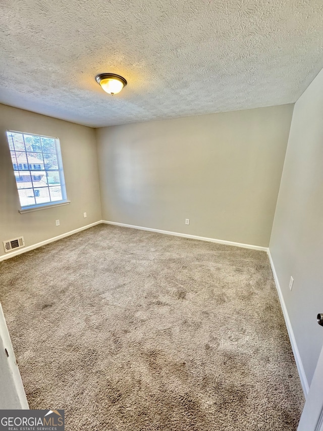 spare room featuring baseboards, visible vents, a textured ceiling, and carpet flooring