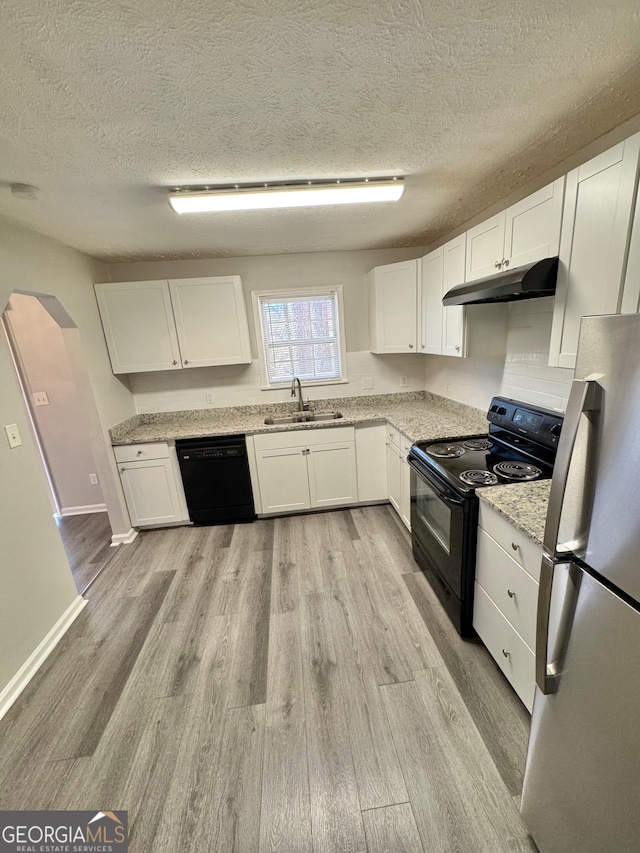 kitchen with arched walkways, white cabinetry, under cabinet range hood, and black appliances