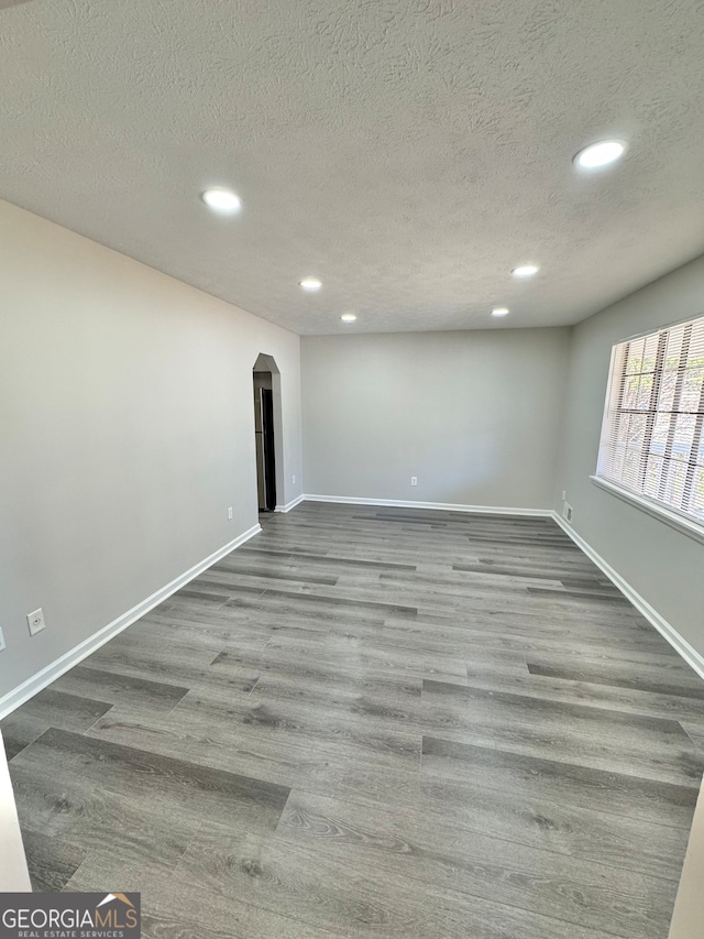 empty room with arched walkways, a textured ceiling, recessed lighting, wood finished floors, and baseboards