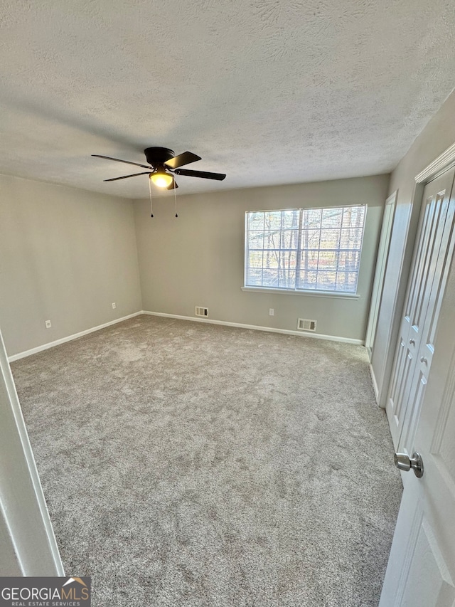 carpeted spare room featuring baseboards, a textured ceiling, visible vents, and a ceiling fan