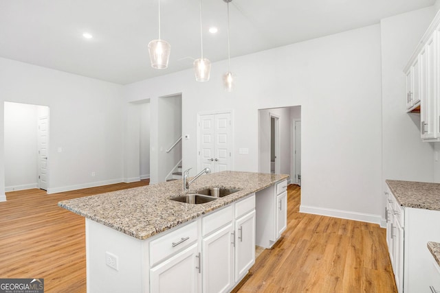 kitchen featuring sink, decorative light fixtures, a kitchen island with sink, light hardwood / wood-style floors, and white cabinets