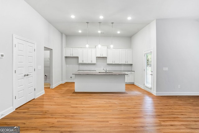 kitchen with sink, white cabinetry, an island with sink, decorative backsplash, and light wood-type flooring