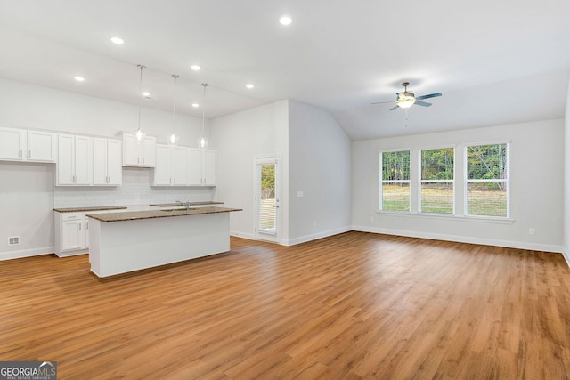 kitchen with an island with sink, white cabinets, decorative backsplash, hanging light fixtures, and ceiling fan