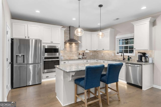 kitchen with a kitchen island, appliances with stainless steel finishes, decorative light fixtures, white cabinets, and wall chimney exhaust hood