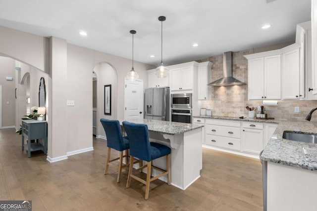 kitchen featuring wall chimney range hood, sink, stainless steel appliances, white cabinets, and a kitchen island