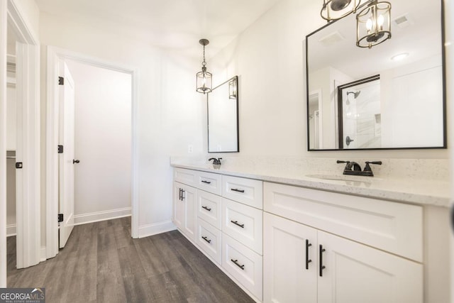 full bath featuring double vanity, baseboards, wood finished floors, a shower with shower door, and a sink