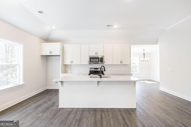 kitchen featuring white cabinetry, vaulted ceiling, light countertops, appliances with stainless steel finishes, and a center island with sink