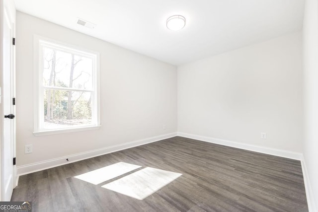 empty room featuring dark wood-style floors, visible vents, and baseboards