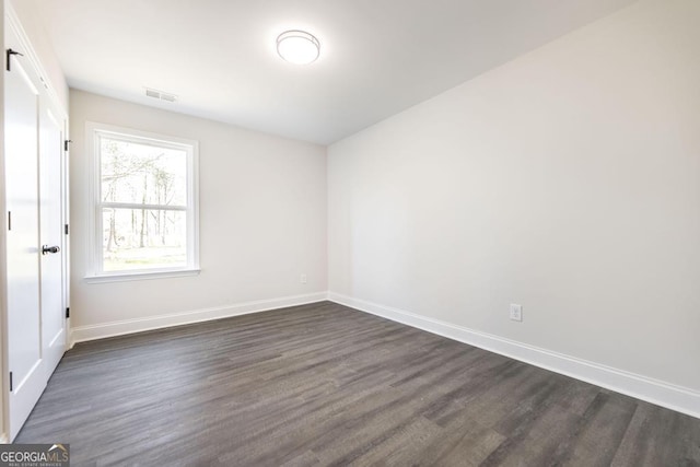 unfurnished room featuring dark wood-style flooring, visible vents, and baseboards