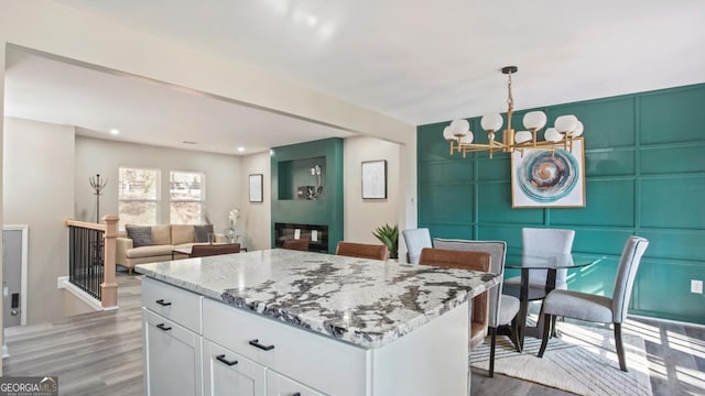 kitchen with dark wood-type flooring, hanging light fixtures, a center island, light stone counters, and white cabinets