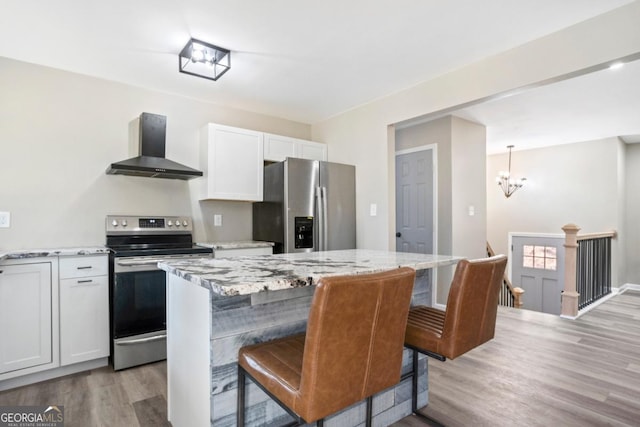 kitchen featuring white cabinets, hanging light fixtures, a center island, stainless steel appliances, and wall chimney exhaust hood